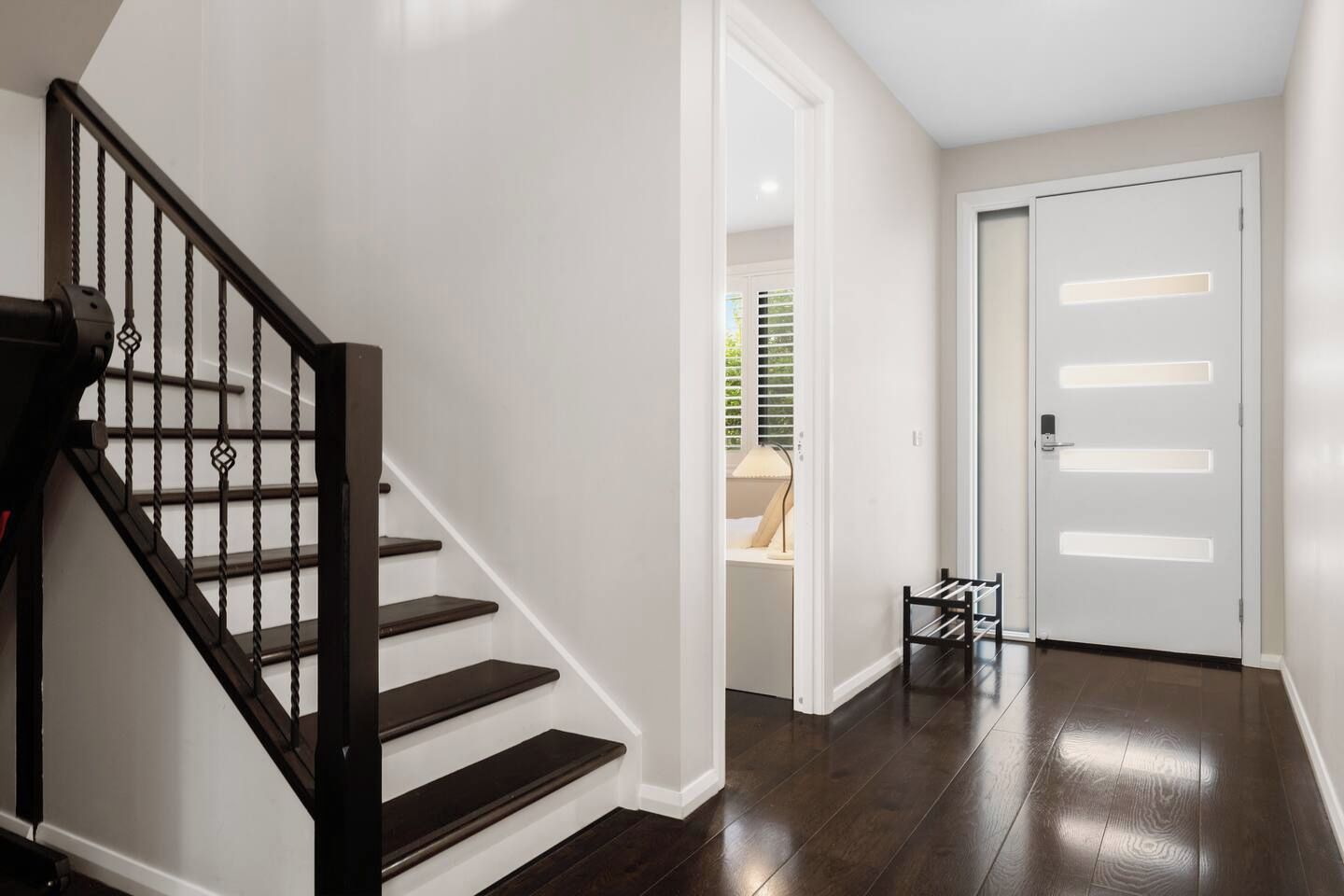 A staircase with a dark wooden finish and a black railing, leading to a room with white walls and a door with a light switch.