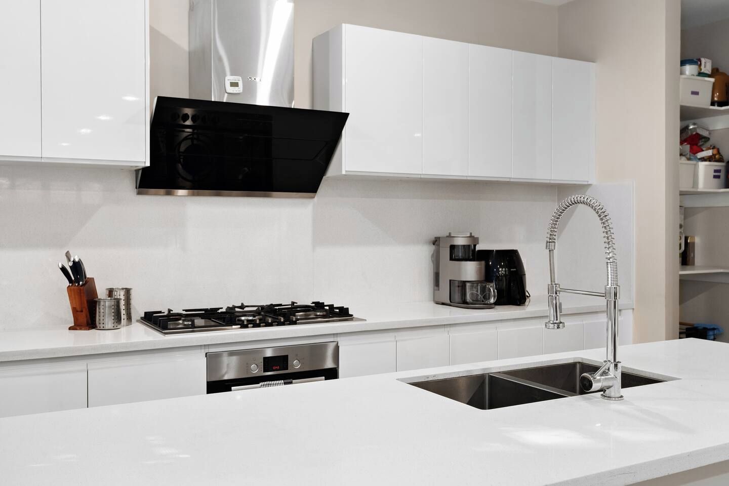 A modern kitchen with white cabinetry, a stainless steel range, a coffee maker, and a built-in dishwasher.