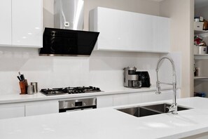 A modern kitchen with white cabinetry, a stainless steel range, a coffee maker, and a built-in dishwasher. - 4BR Doncaster Home | Dual Ensuites & Deck (Doncaster)