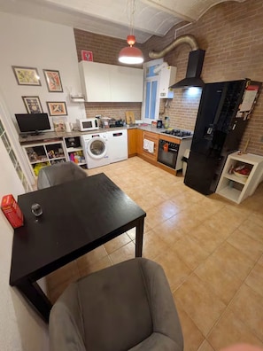 A compact kitchen with a washing machine, microwave, and a stove. - Quiet 3-Bed Eixample Flat, 2 workstations, Balcony & Fast Wi-Fi (Barcelona)