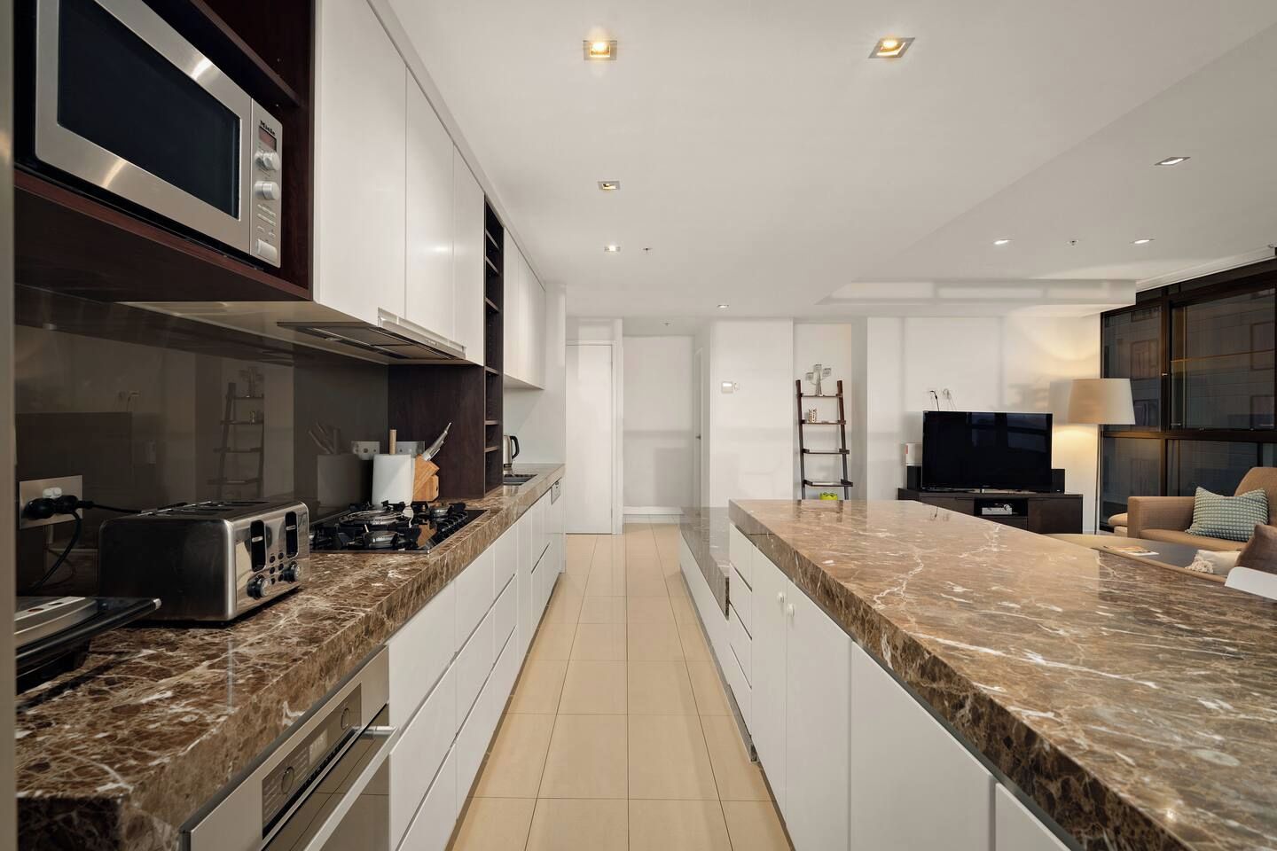 A modern kitchen with a built-in microwave, stove, and toaster. There is a TV and a seating area with a sofa and a lamp.