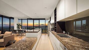 A modern kitchen with a large island, built-in appliances, and a view of the sunset.