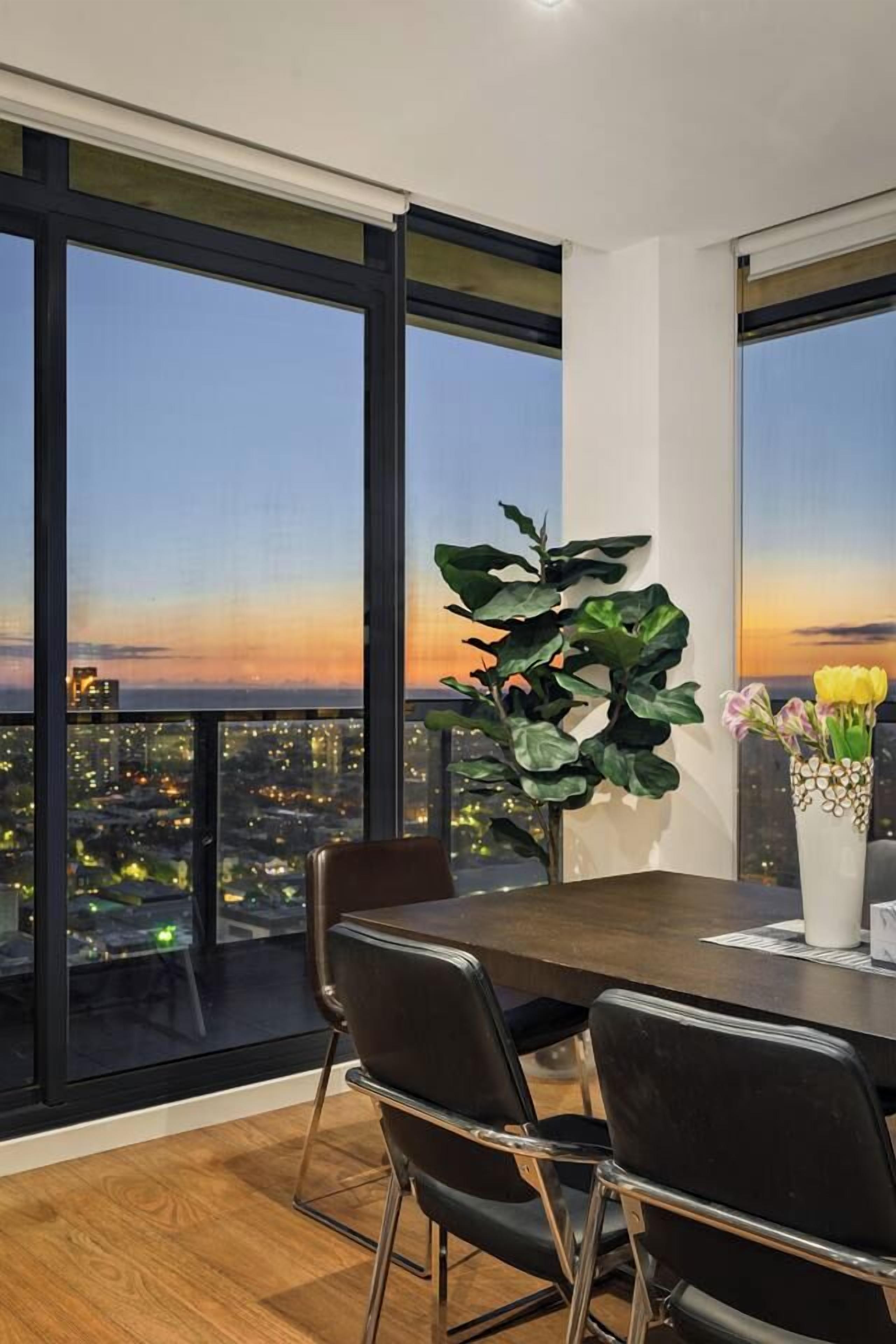 A dining area with a table, chairs, and a view of a cityscape at dusk.