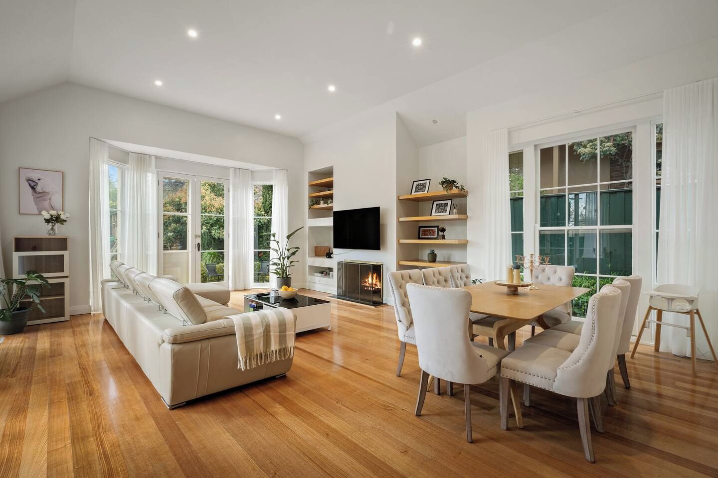 A modern living room with a sofa, dining table, and chairs, a flat-screen TV, and a fireplace.
