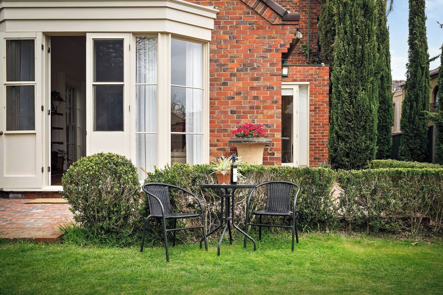 A corner bay window with a white frame, a brick wall, and a small patio with two chairs and a table.