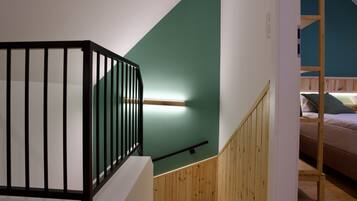 Een trap met een houten leuning en zwarte spijbels, die leidt naar een kamer met een stapelbed en een groene accentmuur.