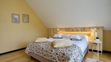 A bedroom with a sloped ceiling, a bed with floral bedding, a bedside table with a lamp, and a small plant.