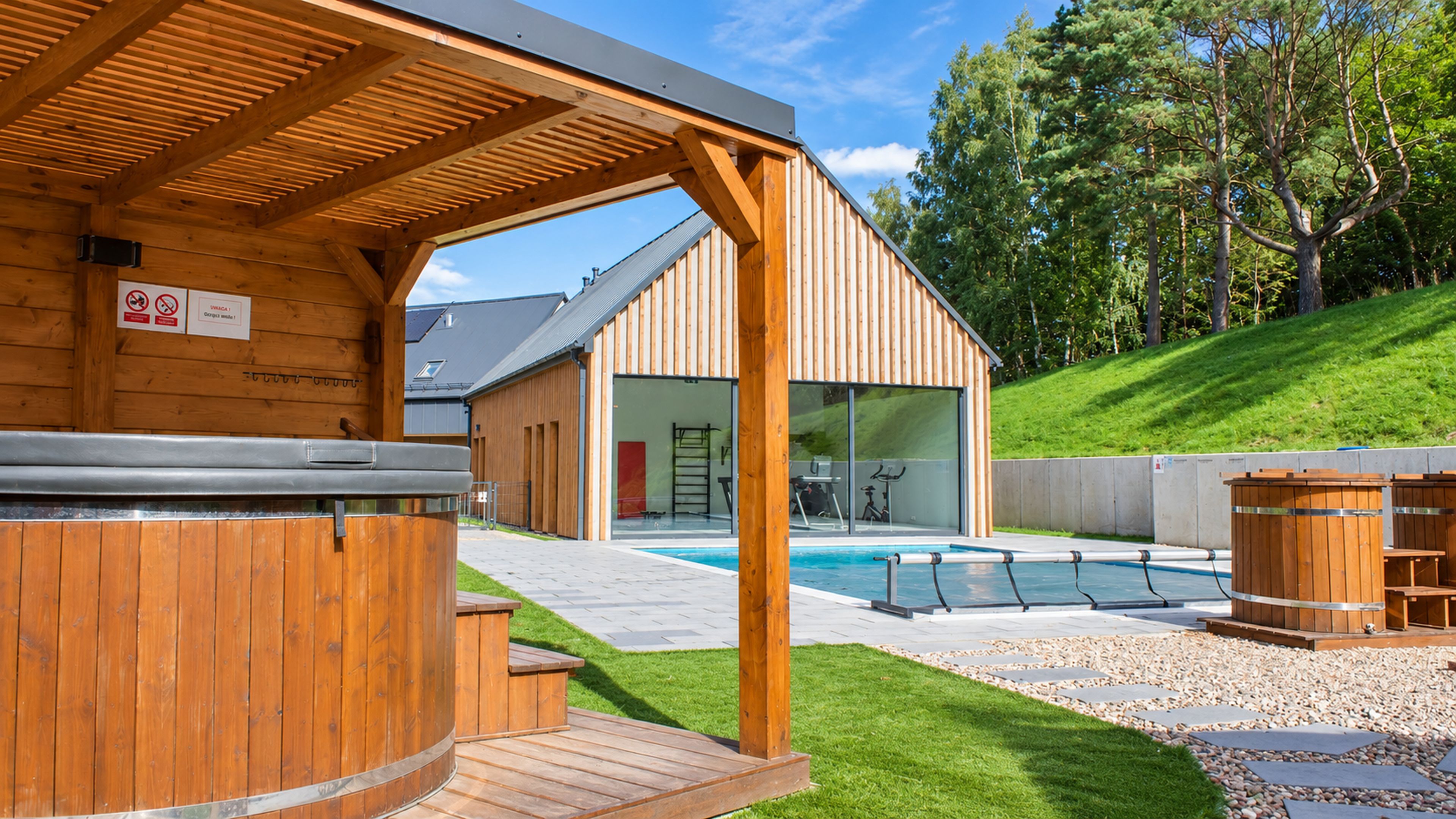 Un espace extérieur en bois comprenant un bain à remous, une piscine, un sauna et un coin salon abrité.