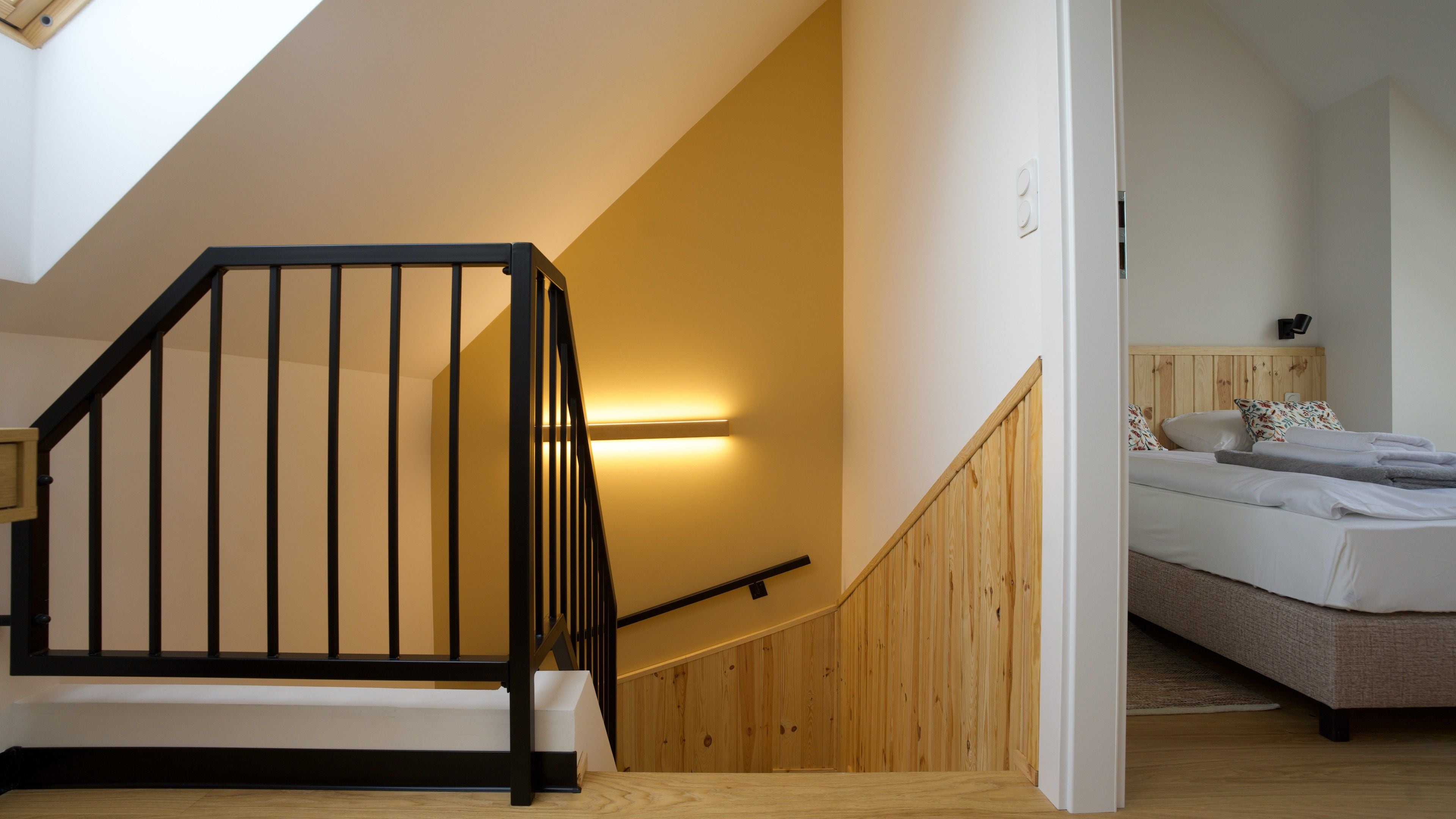Ein Zimmer mit einer Holztreppe, einem Bett mit weißer Bettwäsche und einer wandmontierten Lampe.