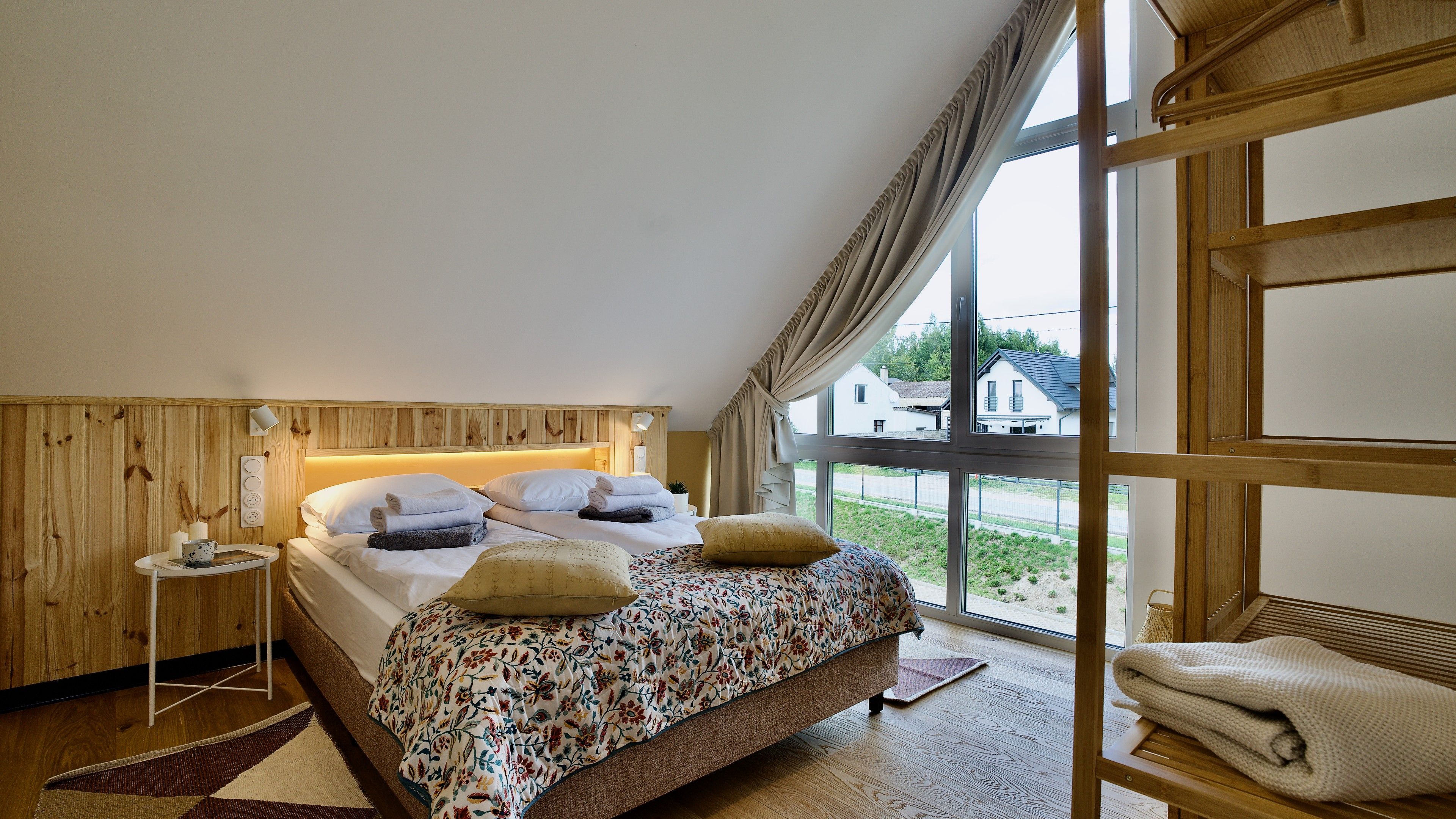 Ein Schlafzimmer mit Bett, Nachttisch, einem Fenster mit Vorhängen und Blick ins Freie.