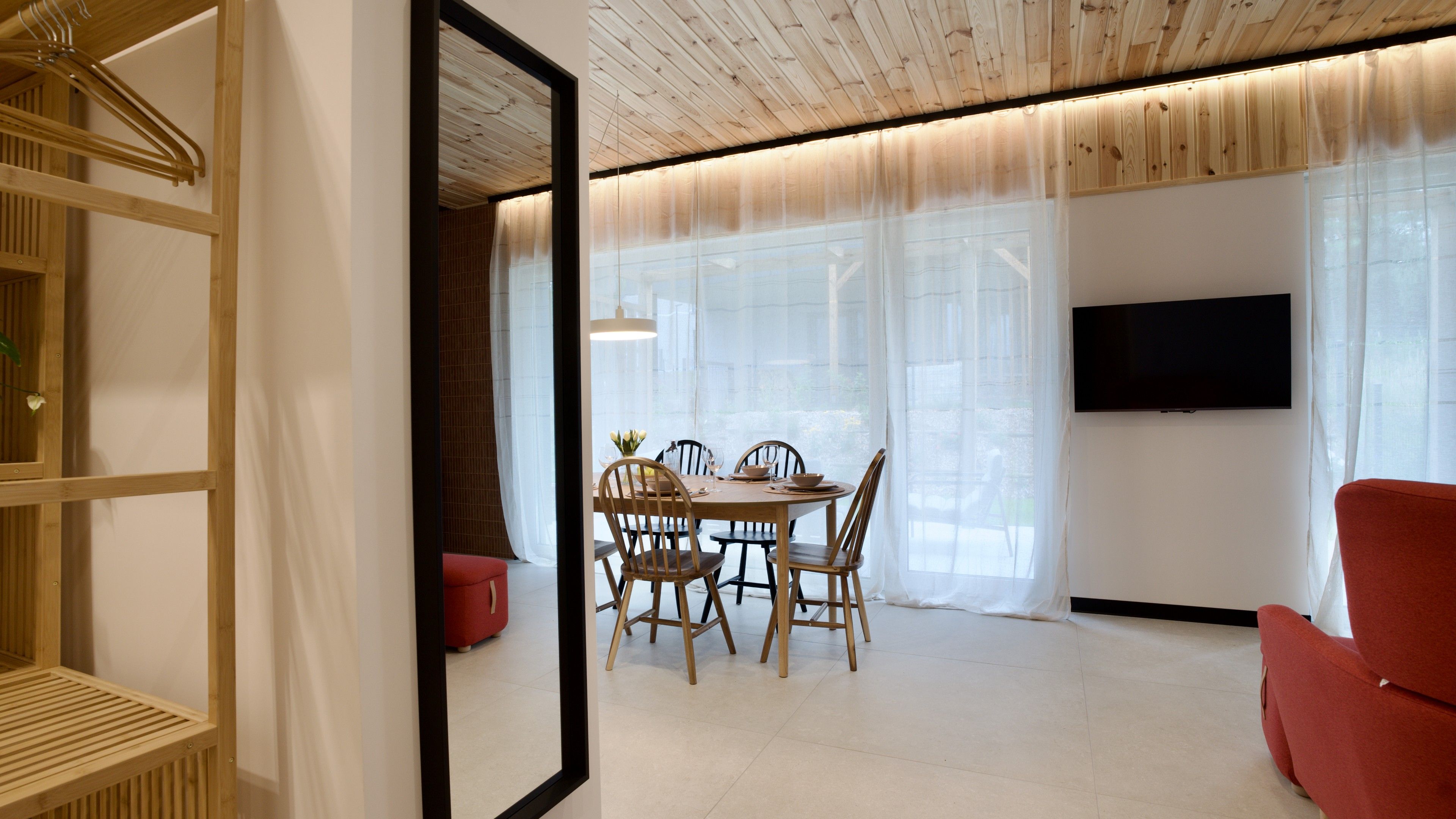 Un salon moderne comprenant un coin repas, un téléviseur fixé au mur et un grand miroir qui agrandit visuellement l’espace.