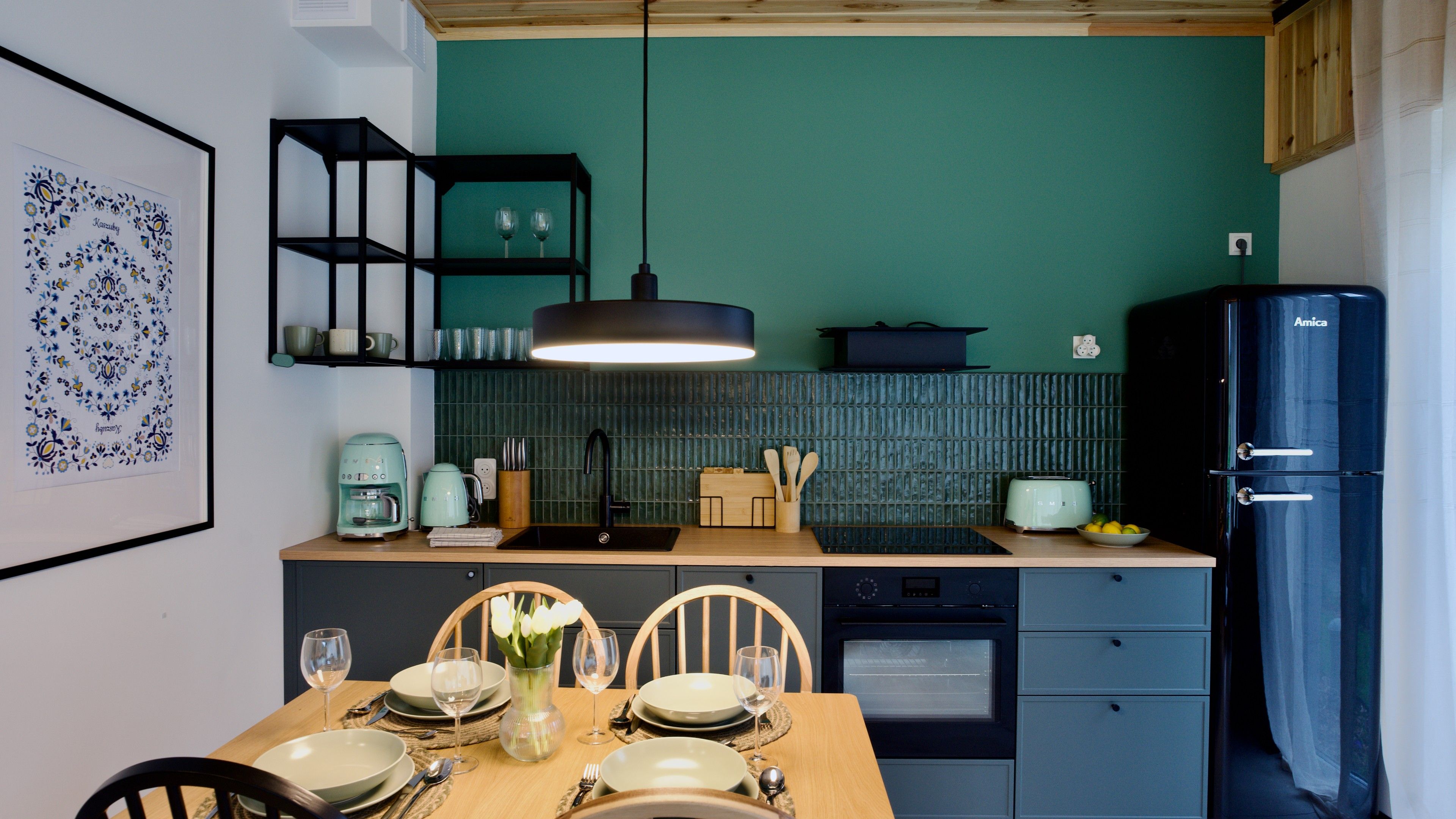 A modern kitchen with a teal backsplash, a black refrigerator, and a dining area set for six.