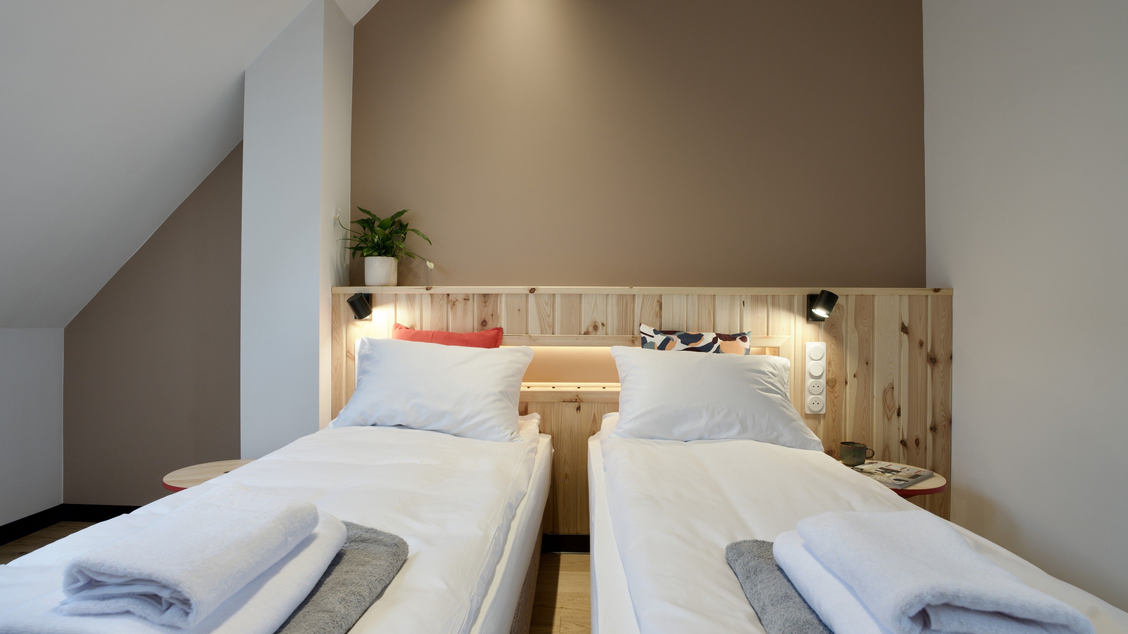 Ein Schlafzimmer mit zwei Einzelbetten, einem Holz-Kopfstück, einem Nachttisch mit Lampe und einer kleinen Topfpflanze.