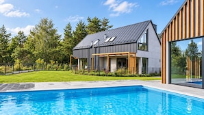 Uma casa moderna com piscina, cercada por um gramado bem cuidado e árvores.