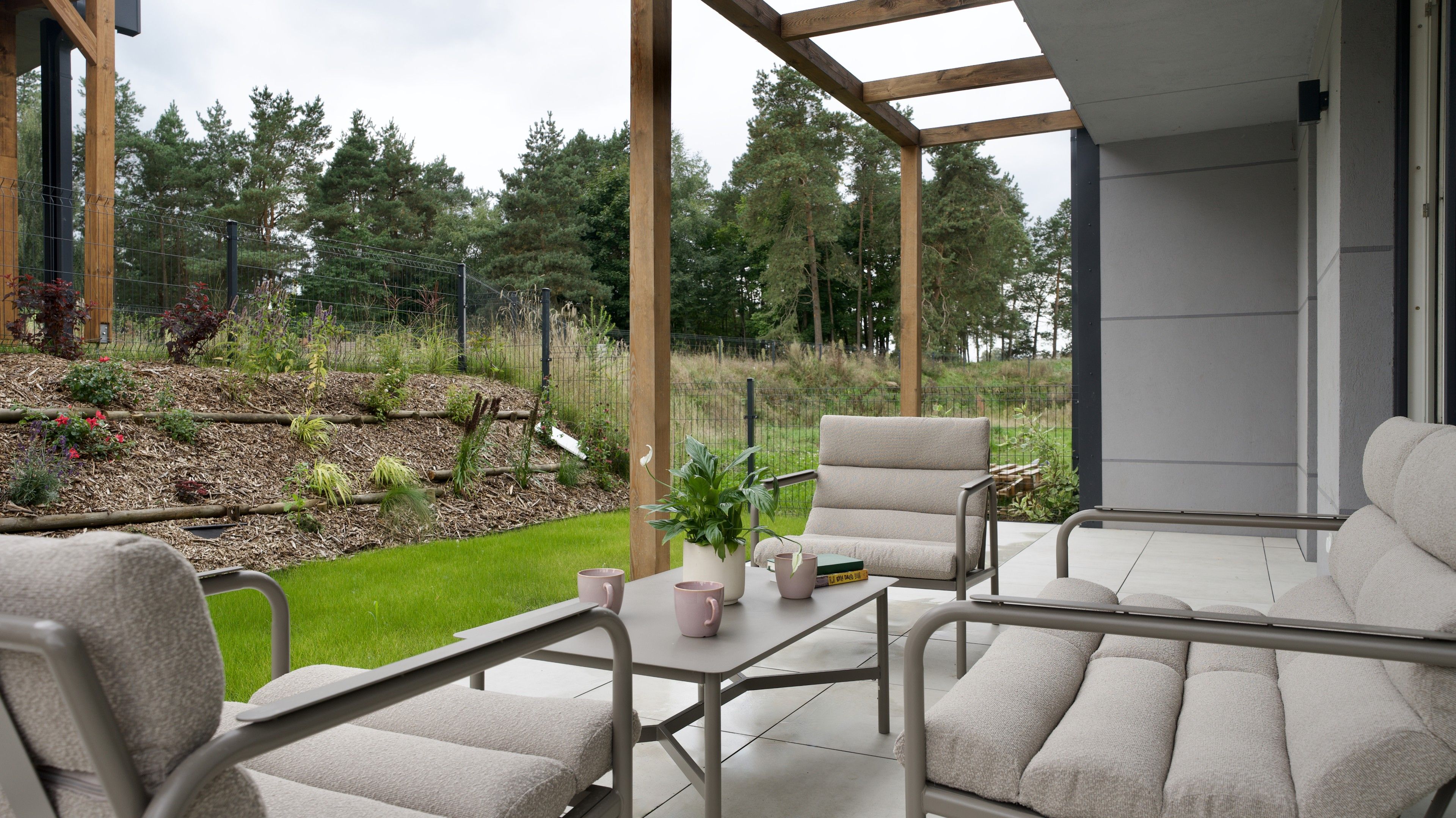 A patio with outdoor furniture, a table with a potted plant, and a view of a landscaped garden.