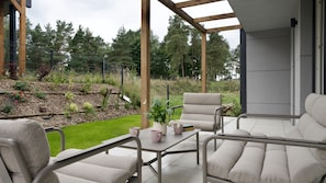 A patio with outdoor furniture, a table with a potted plant, and a view of a landscaped garden.