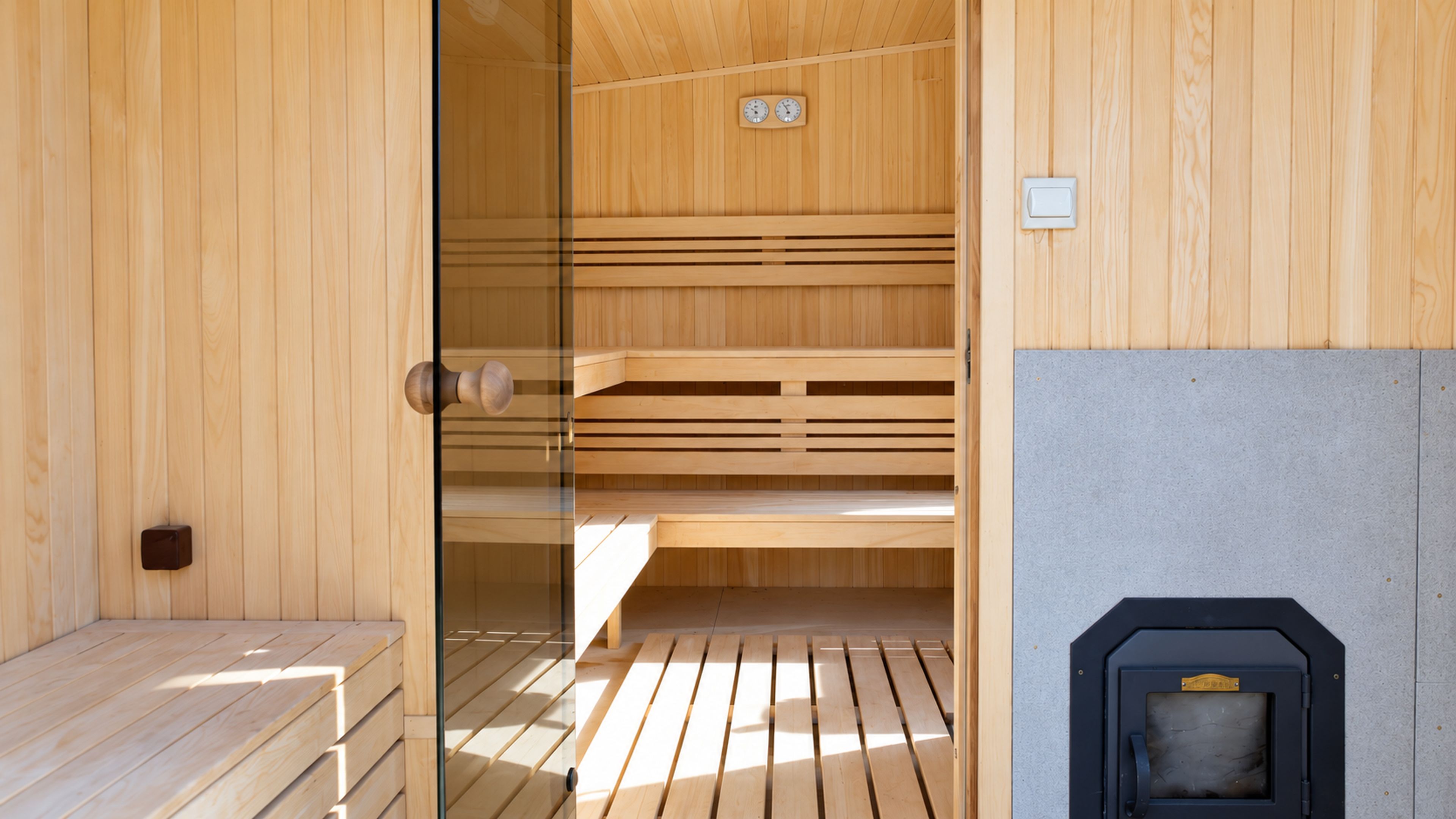 Una sala de sauna con bancos de madera, una puerta de cristal y un calentador de sauna.