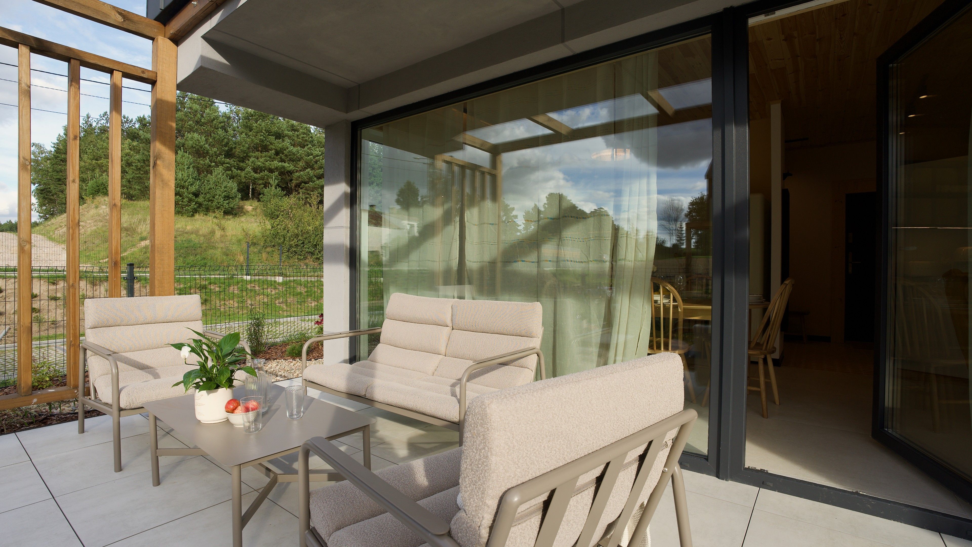 Un área de estar al aire libre, moderna, con una mesa y sillas de vidrio, una planta en maceta y vistas del paisaje circundante.