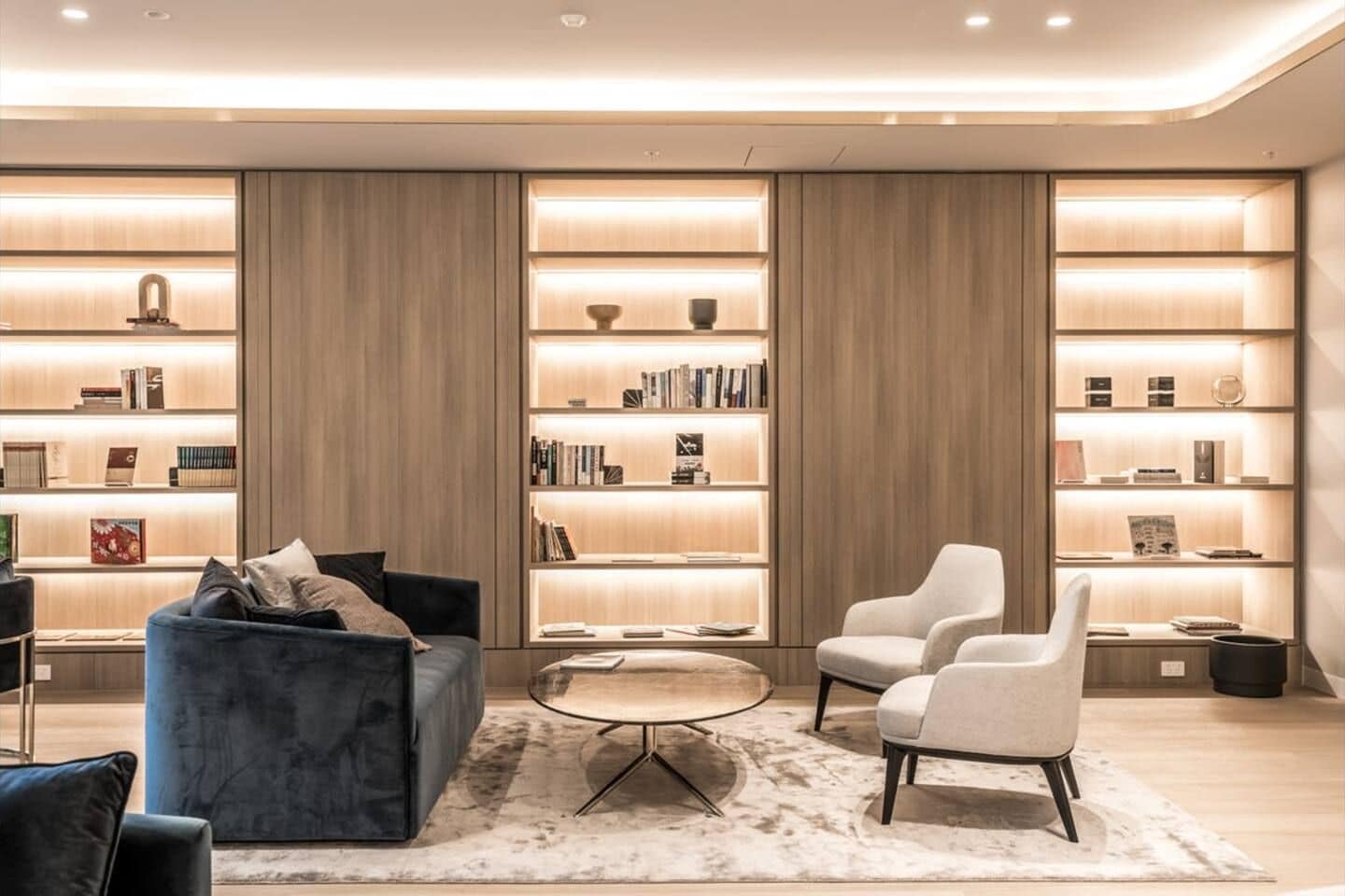 A modern living room with a blue sofa, a round coffee table, and two armchairs. There are two large bookshelves filled with books and decorative items.