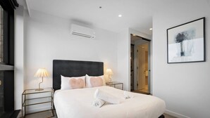 A hotel room with a large bed, two bedside lamps, an air conditioning unit, a glass door leading to a bathroom, and a framed abstract painting on the wall. - Sky One 3BR, 4 Min Walk to Box Hill Station - Apartment (Box Hill)