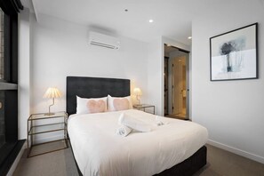 A hotel room with a large bed, two bedside lamps, an air conditioning unit, a glass door leading to a bathroom, and a framed abstract painting on the wall. - Sky One 3BR, 4 Min Walk to Box Hill Station - Apartment (Box Hill)