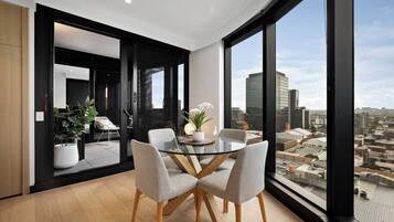 A modern dining area with a glass table and chairs, a potted plant, and a city view through large windows.