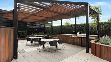 An outdoor patio with a wooden pergola, a grill station, and a seating area with tables and chairs.