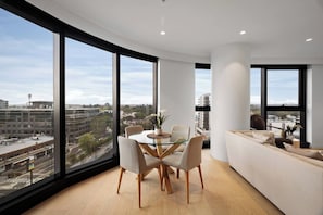 A modern interior with a dining area, a sofa, and large windows offering a city view. - Sky One 3BR, 4 Min Walk to Box Hill Station - Apartment (Box Hill)