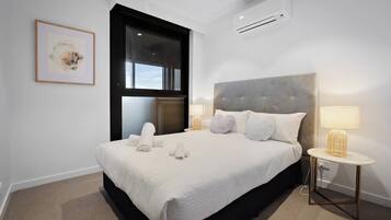A hotel room with a large bed, two bedside lamps, a window, and an air conditioning unit.