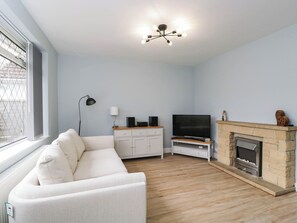 Ein Wohnzimmer mit einem weißen Sofa, einem Fernseher, einem Kamin und einem Fenster mit Jalousien.