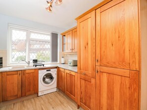 Eine Küche mit Holzausstattung, einer Waschmaschine, einem Spülbecken und einem Fenster mit Blick auf Häuser.