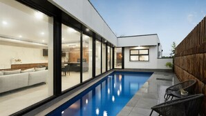 A modern house with a swimming pool, a dining area, and a living room with a sofa. - Grand Designer 5BR Home with Pool | Balwyn (Balwyn North)