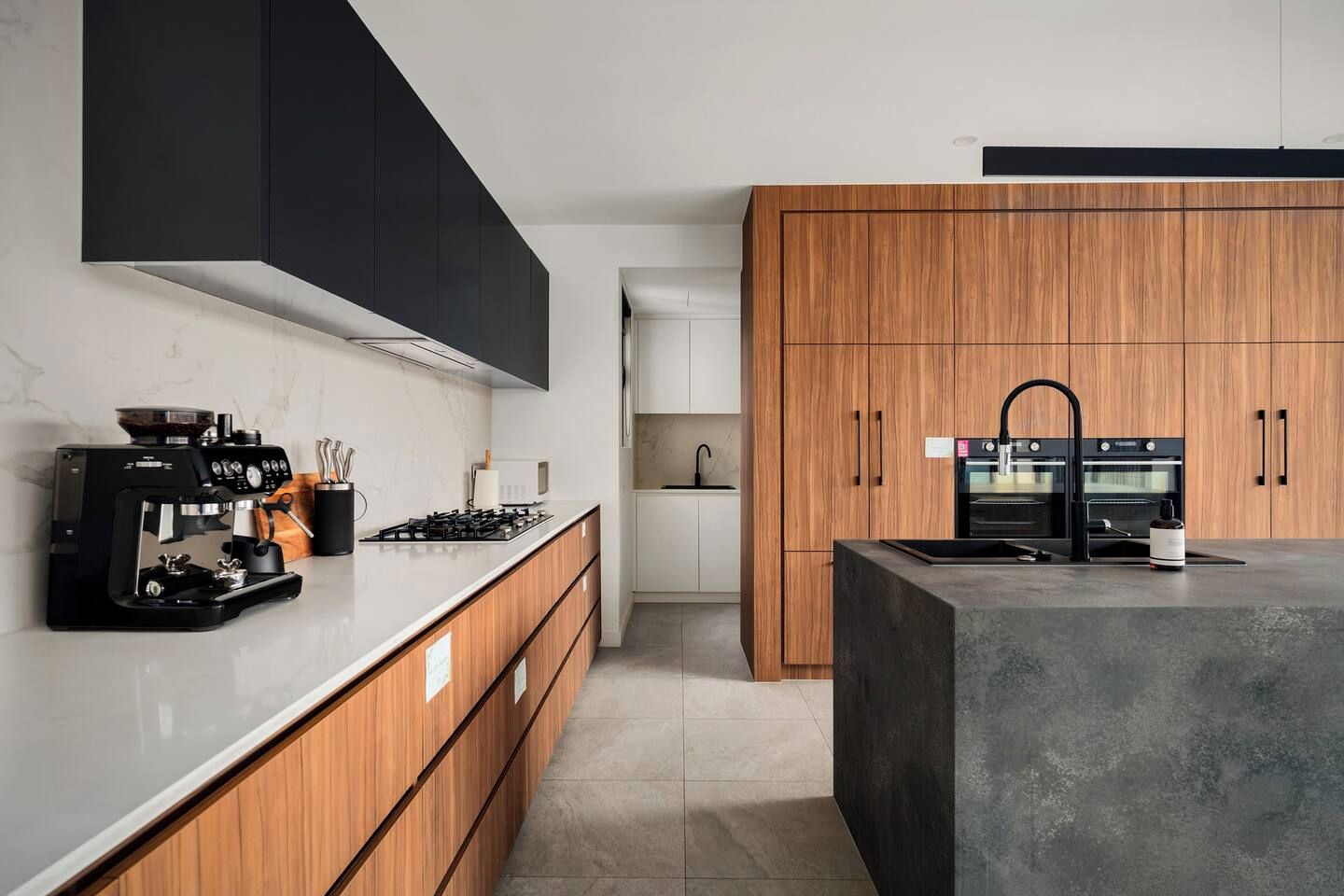 Cozinha moderna com máquina de café expresso embutida, uma ilha grande com pia e armários de madeira.
