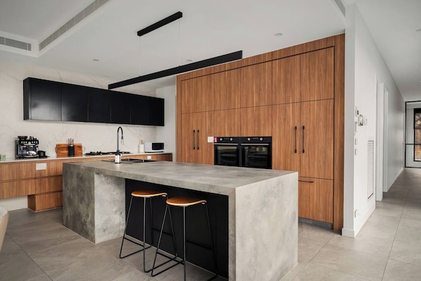 A modern kitchen with a central island, wooden cabinets, and built-in appliances. - Grand Designer 5BR Home with Pool | Balwyn (Balwyn North)