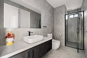 Un bany modern amb un mirall gran, un lavabo blanc, armaris de fusta fosca i un envà de dutxa de vidre.