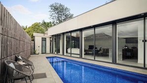 A modern house with a swimming pool, outdoor furniture, and large glass doors leading to a patio area. - Grand Designer 5BR Home with Pool | Balwyn (Balwyn North)
