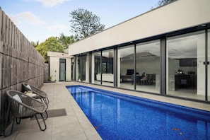 A modern house with a swimming pool, outdoor furniture, and large glass doors leading to a patio area. - Grand Designer 5BR Home with Pool | Balwyn (Balwyn North)