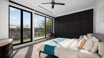 A modern bedroom with a large bed, a ceiling fan, and a view of the outdoors through floor-to-ceiling windows.