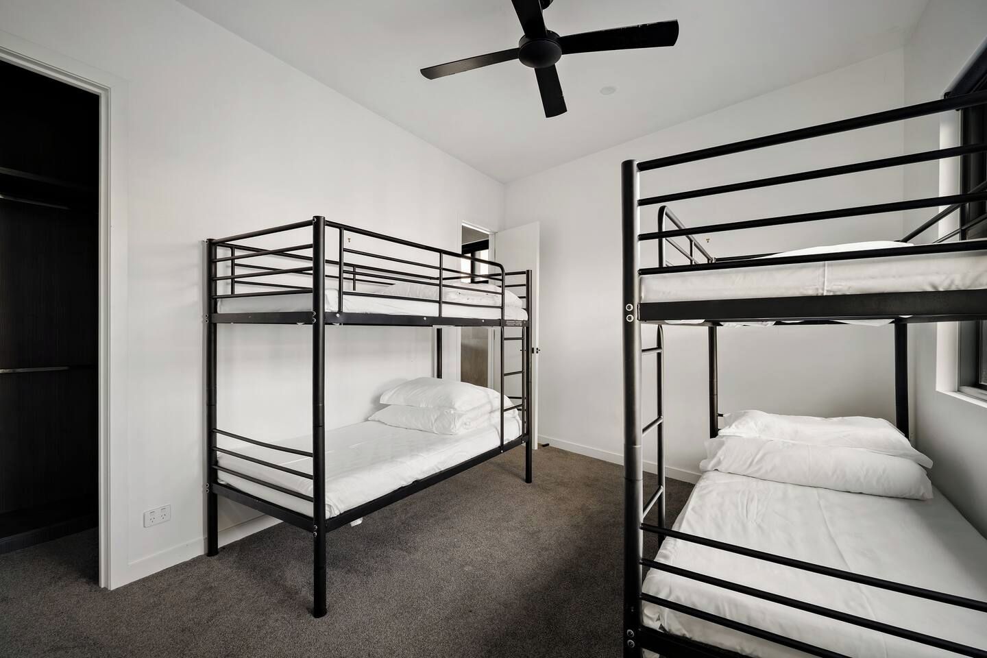 Quarto com duas beliches, um ventilador de teto e uma janela.