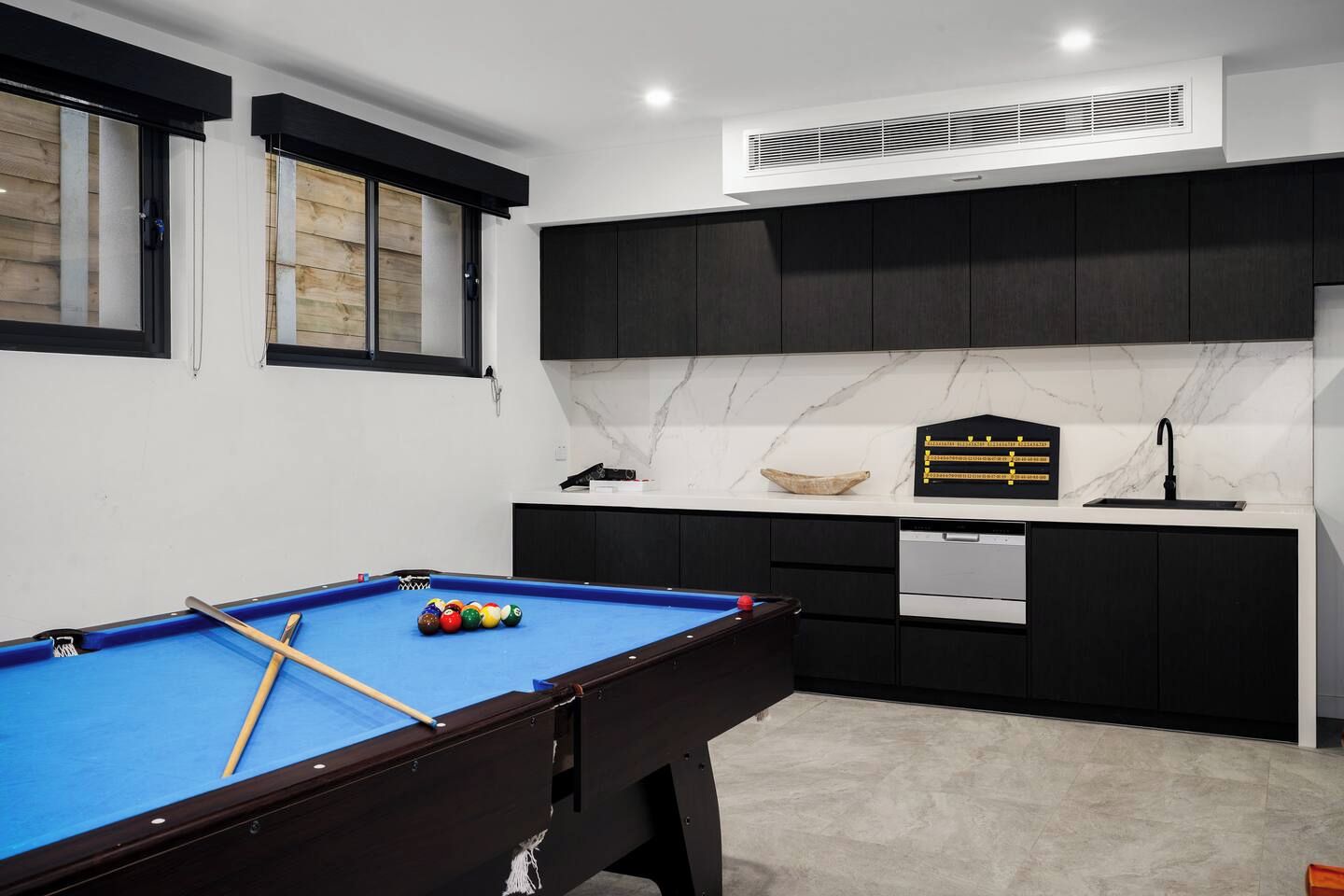 A modern kitchen with dark cabinets, a marble countertop, and a built-in dishwasher.