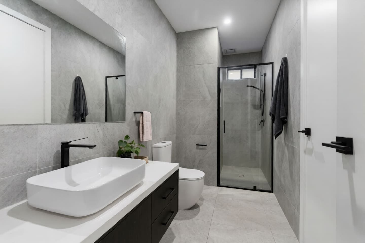 A modern bathroom with a large white sink, a toilet, and a glass-enclosed shower.