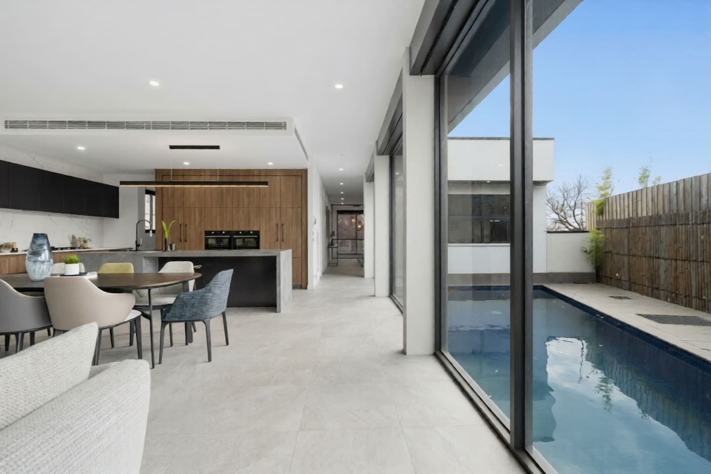 Eine moderne Küche mit Holzausstattung, ein Essbereich mit Tisch und Stühlen sowie ein Haus mit angrenzendem Schwimmbad.