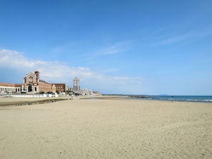 A wide sandy beach with a large building featuring a clock tower and a tall structure in the background. - Stunning  villa for 6 people with A/C, TV and pets allowed (Anzio)