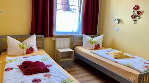 Habitación doble con dos camas, cada una con ropa de cama y almohadas estampadas con motivos florales, una mesita de noche pequeña y una ventana con cortinas.