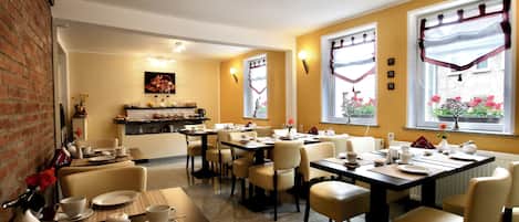 Comedor con varias mesas y sillas, un mostrador de buffet y vistas a flores a través de las ventanas.