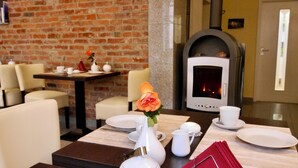 Un comedor con pared de ladrillo, chimenea y una mesa lista para dos personas, con vajilla blanca.
