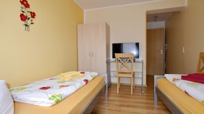 Una habitación con dos camas, un escritorio con silla, un televisor y un armario.