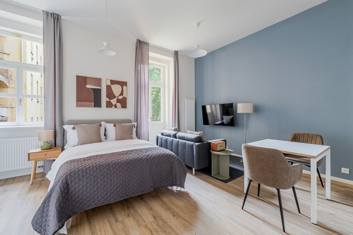 A modern bedroom with a bed, bedside table, lamp, and a desk with a chair.
