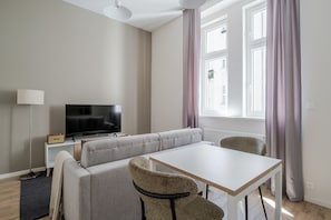A modern living room with a sofa, a TV, a table, and a chair. - Letná Residence by Blueground (Prague)