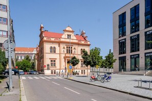 A historic building with classical architecture, a modern adjacent building with signage, and a clear street with parked cars and bicycles. - Letná Residence by Blueground (Prague)